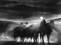 black and white photograph of horses running in the fog with full moon rising behind them