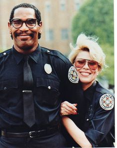 a man and woman dressed in police uniforms posing for a photo with their arms around each other