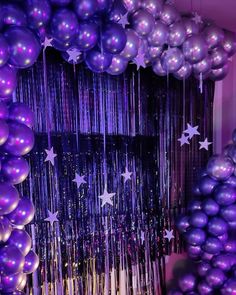 purple balloons and streamers are hanging from the ceiling in front of a curtain that has stars on it