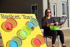 a woman sitting on a chair next to a basket toss sign with plastic cups in front of it