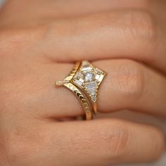 a woman's hand wearing a gold ring with two diamonds on it and a diamond set in the middle