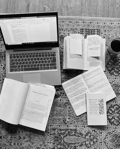 an open laptop computer sitting on top of a rug covered in books and papers next to a cup of coffee