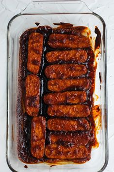 a glass dish filled with meat covered in bbq sauce on top of a white table