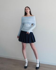 a woman is posing in front of a white wall wearing a blue top and black skirt