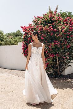 a woman in a wedding dress standing next to a bush with flowers on the side