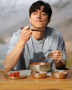 a man sitting at a table eating food with chopsticks in front of him