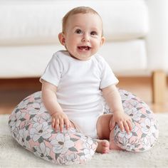 a smiling baby sitting on a flowered bean bag chair in front of a white couch