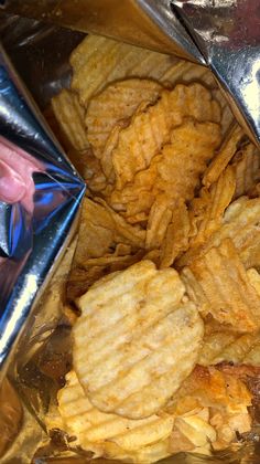 a pile of potato chips sitting on top of a metal tray next to a person's hand