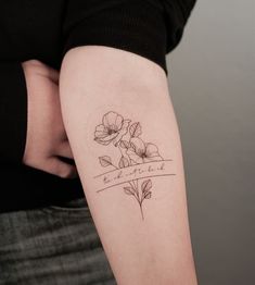 a woman with a tattoo on her arm that has flowers and the words love is written in cursive writing