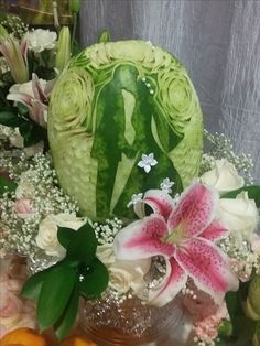 a watermelon carved to look like a bride and groom with flowers in the background