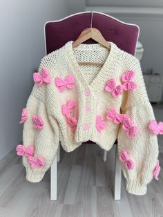 a white sweater with pink flowers on it and a purple chair in the back ground