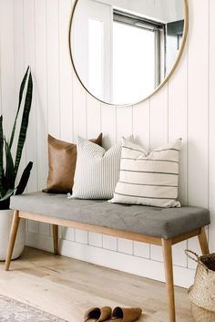 a wooden bench with pillows and a round mirror on the wall