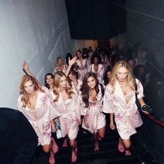 a group of women in pink dresses walking down a flight of stairs with their arms up