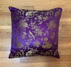 a purple and gold pillow sitting on top of a wooden floor next to a wall