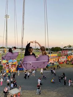 two people sitting on swings in the middle of an amusement park while others walk around