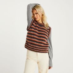 a woman is wearing a striped sweater and white pants with her hand on her head