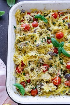 a casserole dish filled with pasta, tomatoes and basil garnished with parmesan cheese