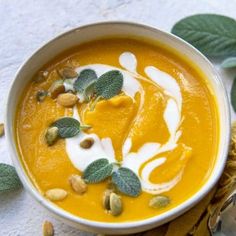 a white bowl filled with carrot soup next to some leaves and nuts on the table