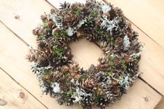 a wreath made out of pine cones and evergreen needles on a wooden surface with snow flakes