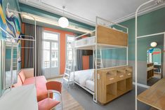 a room with bunk beds, desk and chairs next to each other in front of a window