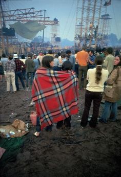 people standing around in the mud at an outdoor music festival, some wrapped up and others looking on