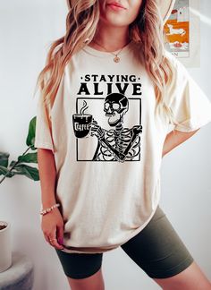 Staying Alive Shirt, Trendy Coffee Shirt, Funny Skeleton T-Shirt, Coffee Lovers Gift Skull Vintage Halloween Tee  Sizing and Color Information: Our shirts are made to order specially for you. For this reason, we don't accept returns or exchanges. To ensure the perfect fit, please refer to our color and size charts before placing your order. If you have any questions, don't hesitate to send us a message to clarify sizing or colors. HOW TO ORDER MULTIPLES: 1. Select your size and color in the drop Coffee Lovers Gift, Skeleton T Shirt, Funny Skeleton, Coffee Shirt, Coffee Tshirt, Display Picture, Coffee Shirts, Halloween Tees, Staying Alive