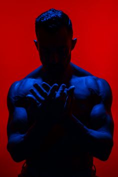 a man with his hands together in front of a red and blue background that looks like he is holding something