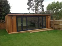 a small wooden shed with sliding glass doors on the outside and grass in the yard