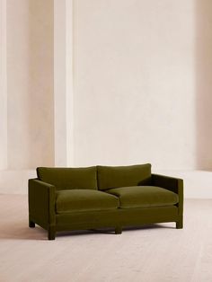 a green couch sitting on top of a hard wood floor next to a white wall