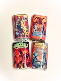 four canisters with godzilla comics on them are lined up against a white background