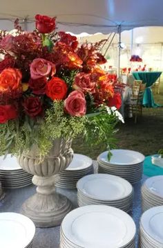 a vase filled with lots of red and orange flowers next to white plates on a table