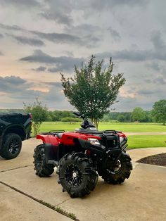 a red four - wheeler parked in front of a black truck on the side of a road