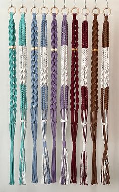 several different colored braids hanging from hooks on a white wall with metal rings attached to them