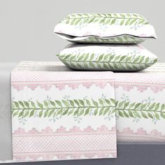 three pillows are stacked on top of each other in front of a white bed with pink and green designs