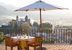 a table with two chairs and an umbrella on top of a balcony overlooking the city