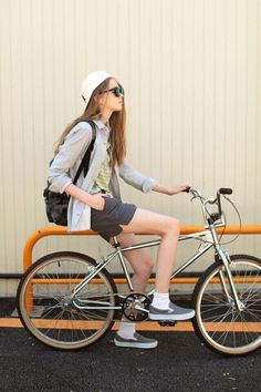 a woman sitting on top of a bike next to a yellow fence and wearing a white hat