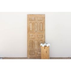 a vase with flowers in it sitting next to a wooden door on the floor near a white wall