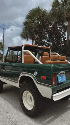 a green and white pick up truck parked in a parking lot next to palm trees