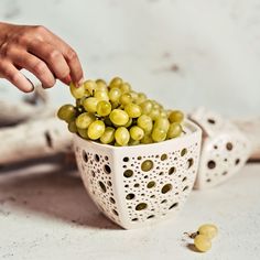 a person picking grapes from a white bowl