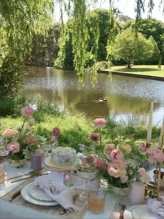 a table set up with flowers and candles for an outdoor dinner by the lake in summer