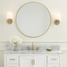 a bathroom vanity with a round mirror above it and two lights on the wall behind it