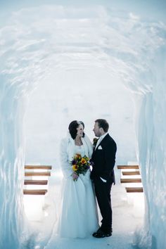 a bride and groom are standing in an ice tunnel at their wedding day, looking into each other's eyes