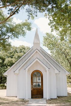 a small white church with a wooden door and steeple on the front, surrounded by trees