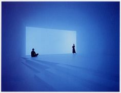 two people sitting in the middle of a room with blue light coming from it and one person standing at the end