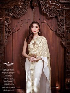 a woman in a white and gold sari standing next to a wooden paneled door