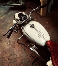 a white motorcycle parked on top of a street next to a red leather seat with writing on it