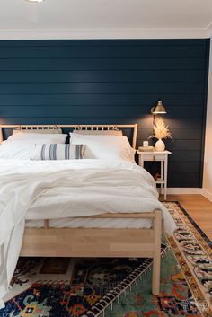 a bed with white sheets and pillows in a bedroom next to a blue accent wall