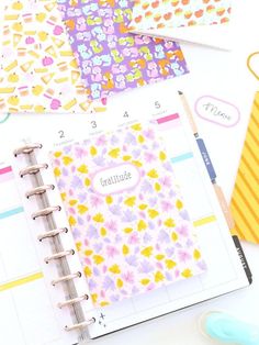 an open planner with flowers on it next to some pens and paper clippings