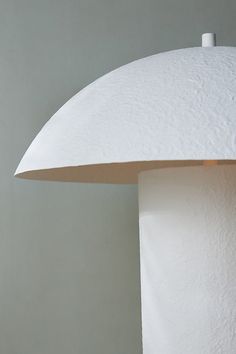 a close up of a white lamp on a table with a gray wall in the background