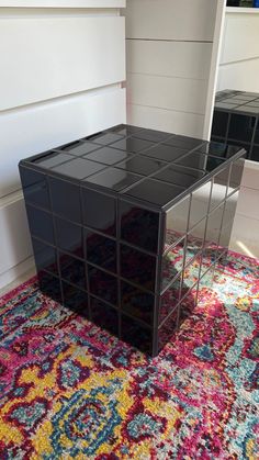 a black table sitting on top of a colorful rug next to a white wall and window